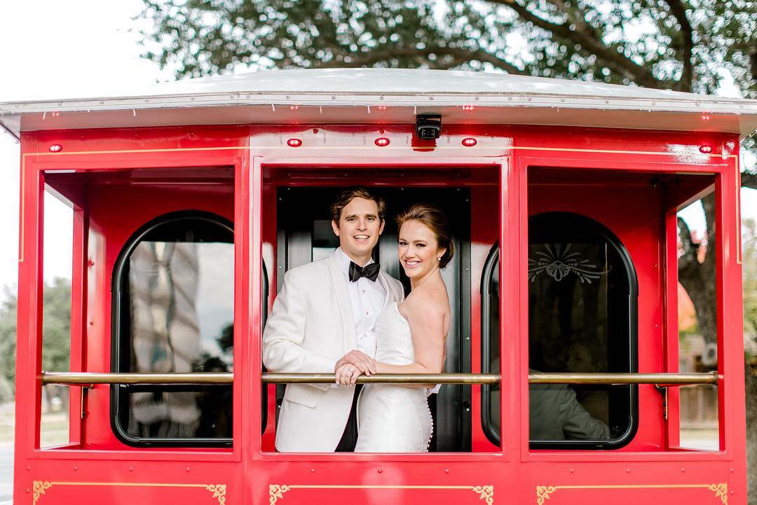 an image of a bride and groom standing on the back of a red trolley