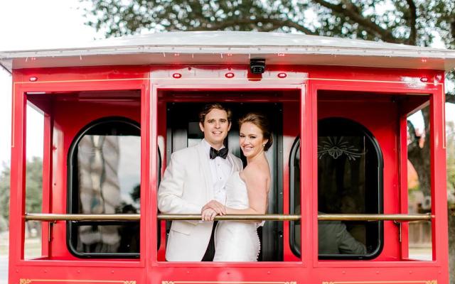 an image of a bride and groom standing on the back of a red trolley